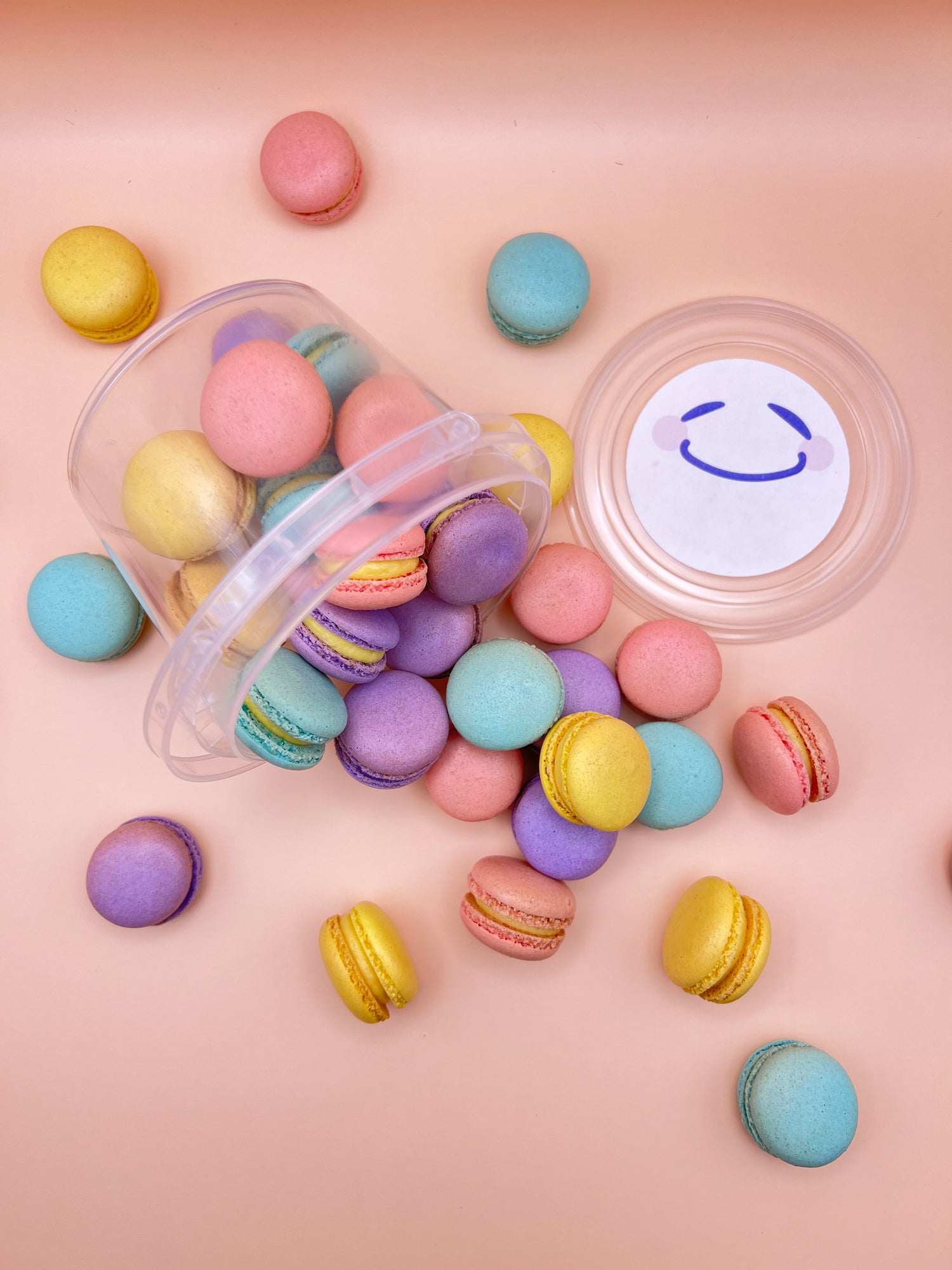 Assorted mini macarons spilling from a bucket on a pink background