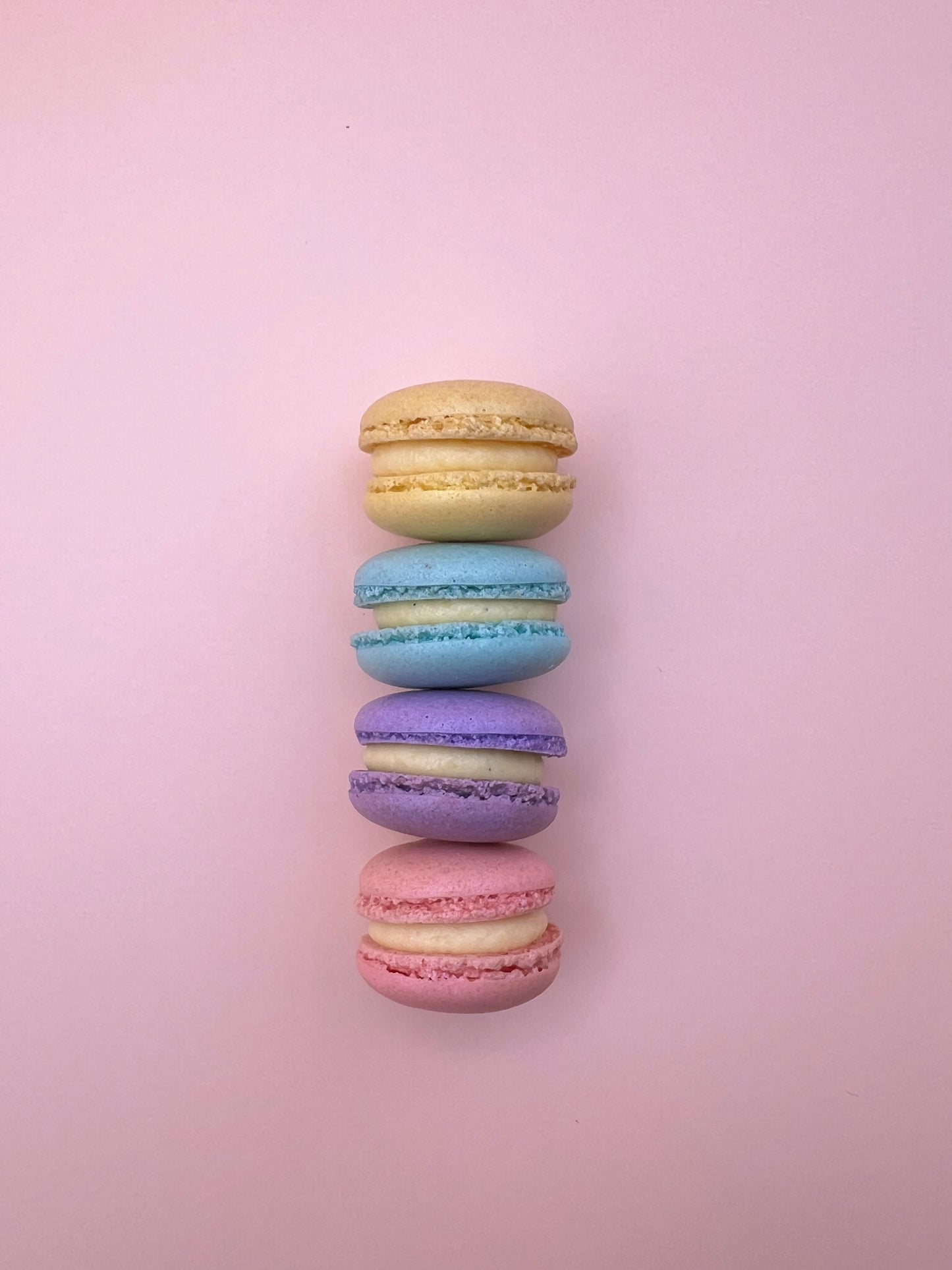 Assorted mini macarons lined up on a pink background