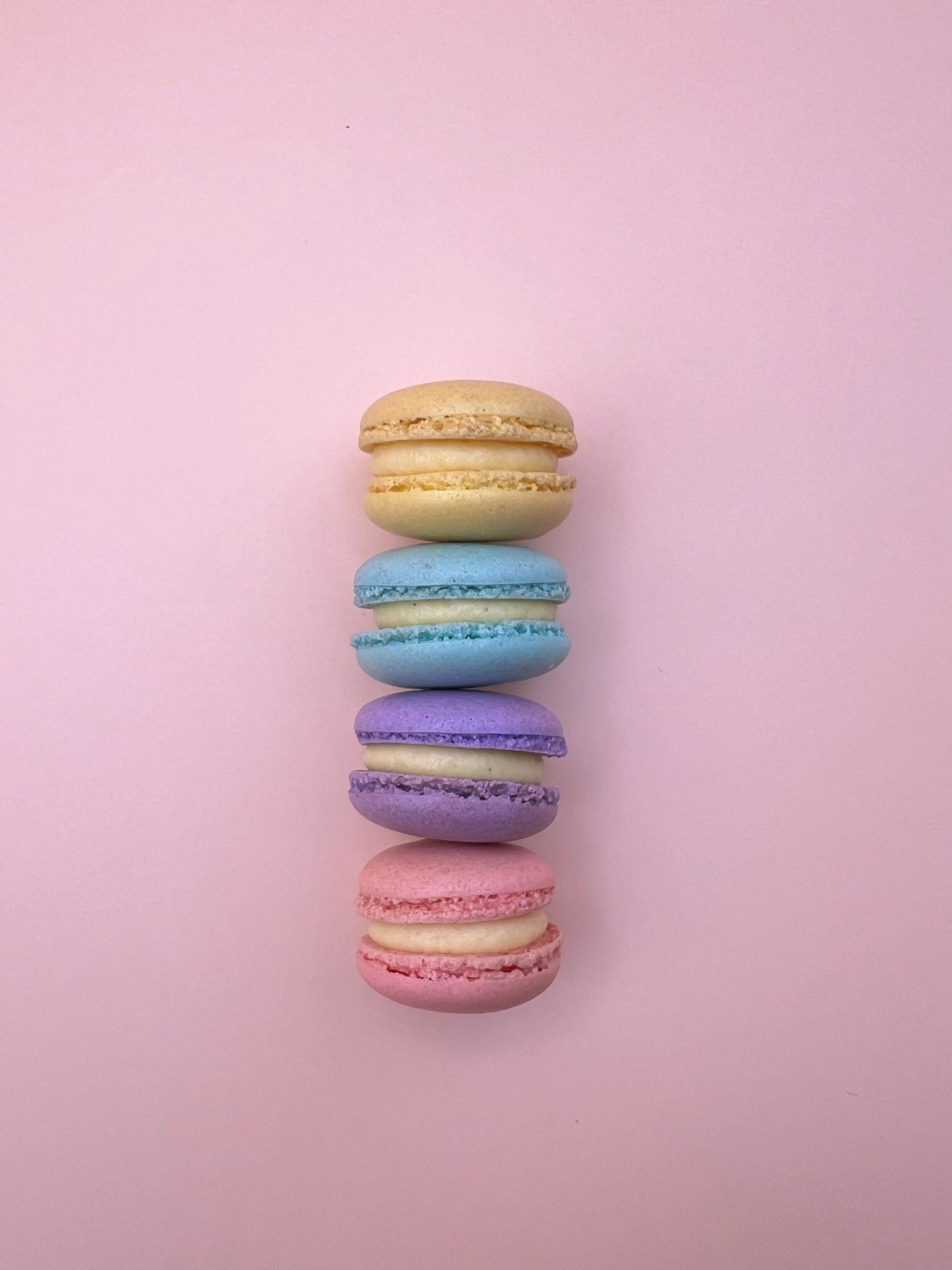 Assorted mini macarons lined up on a pink background