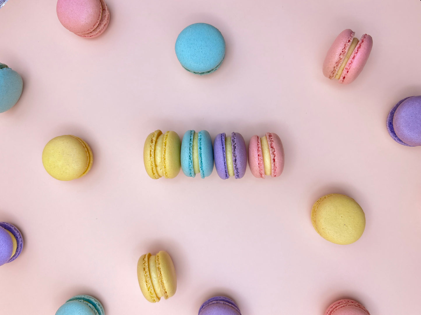 Colorful mini macarons arranged on a light pink background