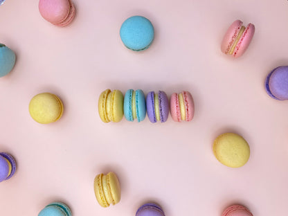 Colorful mini macarons arranged on a light pink background